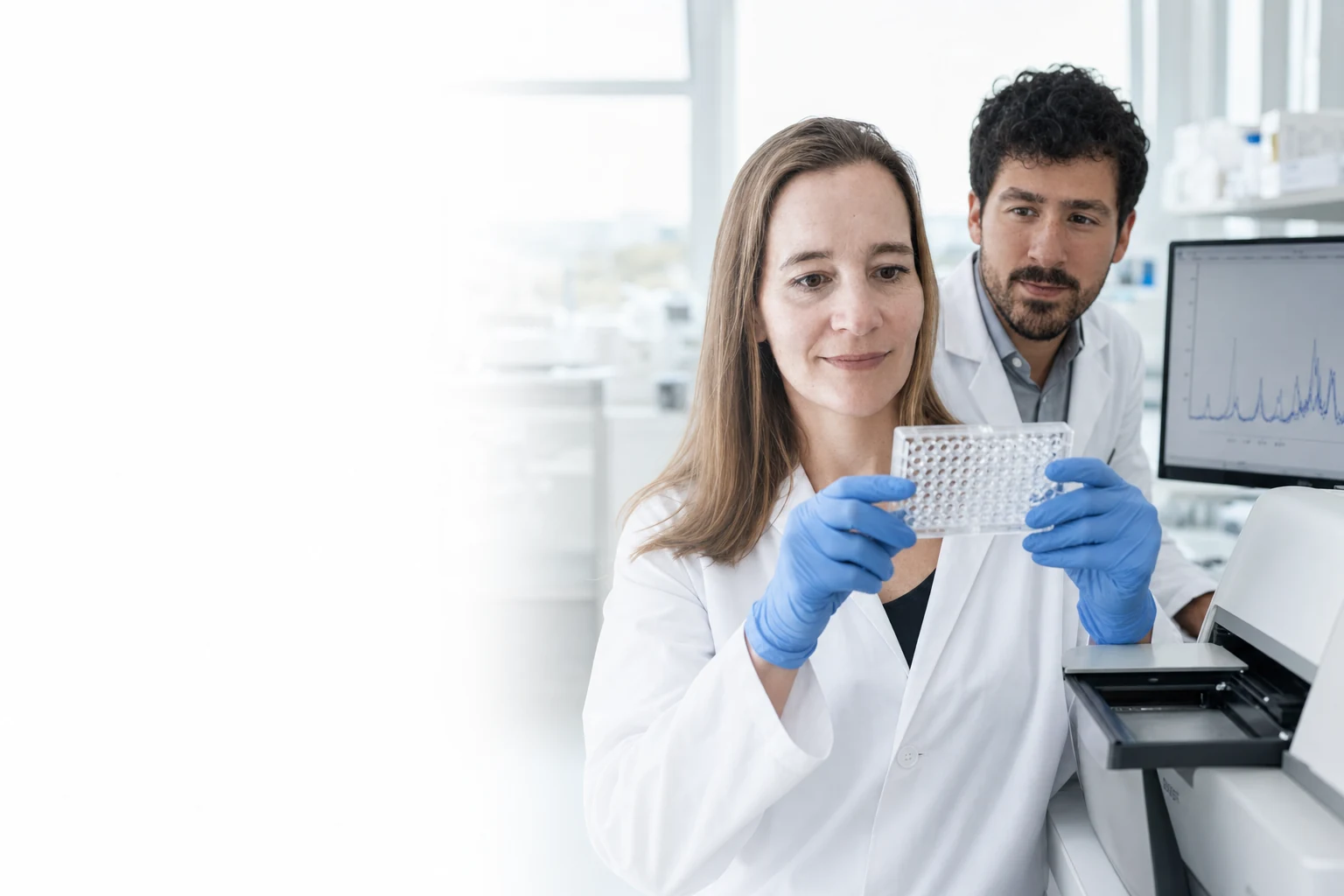 Heidi Derks and Dr. Elia Gamba reviewing a bioassay plate and protein analytics data in a bright laboratory. Illustrative generated image based on approved Peptone team portraits.