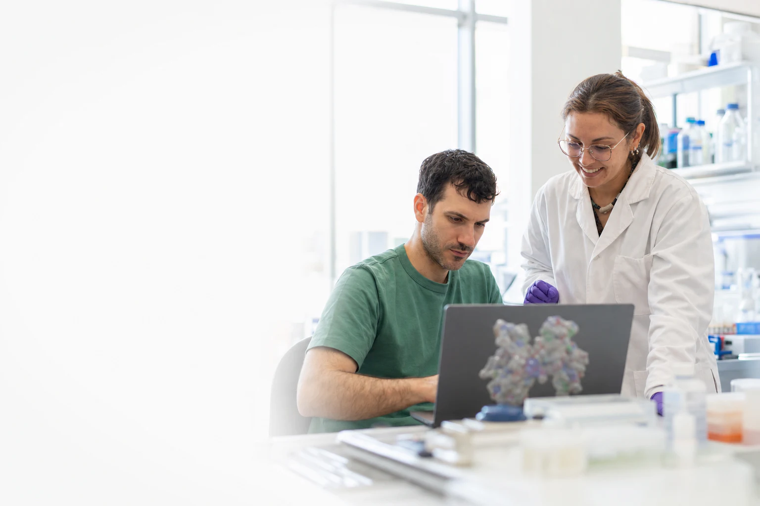 Two Peptone team members collaborating at a computational workstation in a bright laboratory. Illustrative generated image based on Peptone team photographs.