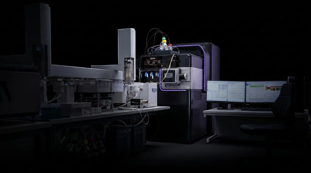 Peptone's HDX-MS system in a dark laboratory, with automated fluidics, the mass spectrometer, and dual analysis monitors.